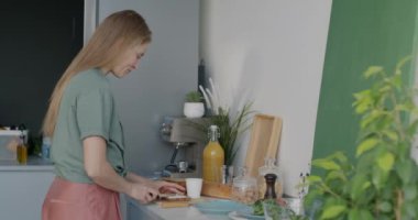 Neşeli genç bayan ev hanımı evde tek başına durup lezzetli peynirli sandviçler hazırlıyor. Yemek hazırlama ve beslenme konsepti.