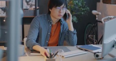 Cep telefonuyla konuşan Asyalı işadamı ofiste masa başında iş tartışıyor. Girişimci ve cep telefonu iletişim kavramı.