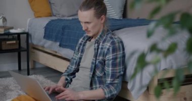 Evde, yatak odasında yerde oturan dizüstü bilgisayarla çalışan serbest çalışan genç bir adam. Serbest çalışma ve mesafe iş konsepti.
