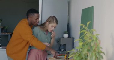 Kadın salata pişirirken, genç adam peynir yemeye çalışıyor sonra da kocaya sarılıp mutfakta eğleniyor. Sağlıklı beslenme ve ilişki kavramı.