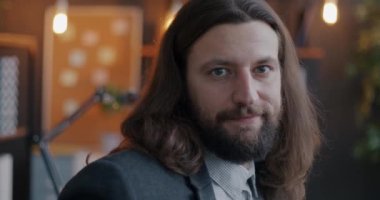 Aydınlatılmış ofiste kameraya bakan yaratıcı saç stiline sahip genç girişimcinin yavaş çekim portresi. İş ve bireysellik kavramı.