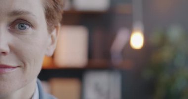 Yarım yüzlü iş kadınının, bulanık ofis arka planında hafif bir gülümsemeyle kameraya baktığı yavaş çekim. Halk ve iş kavramı.