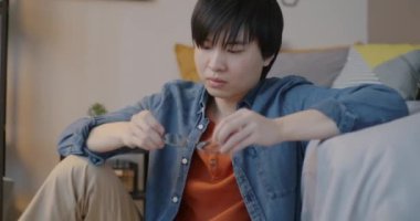 Çekici Asyalı adamın portresi şık gözlükler takıyor ve yatak odasında yere oturmuş kameraya bakıyor. Kişi ve gözlük konsepti.