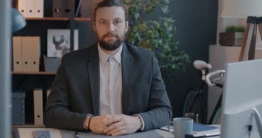 Takım elbiseli bir girişimcinin yavaş çekim portresi ofis odasında oturuyor ve kameraya bakıyor. Başarılı iş ve kariyer fırsatı kavramı.