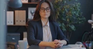 Akşamları ofiste oturan, ciddi yüzüyle kameraya bakan kendine güvenen genç iş kadınının portresi. İş yeri ve yönetici konsepti.