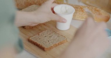 Ekmeğe krem peynir sürerek sandviç yapan kadın elleri mutfakta lezzetli atıştırmalıklar hazırlıyor. Beslenme ve gıda konsepti.