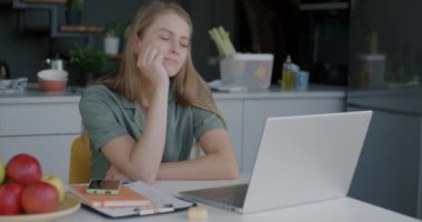 Genç bayan serbest çalışan bilgisayarlı daktilo kullanıyor. Mutfakta oturuyor ve online aktivitelere konsantre oluyor. Serbest meslek ve yerli iş yeri kavramı.