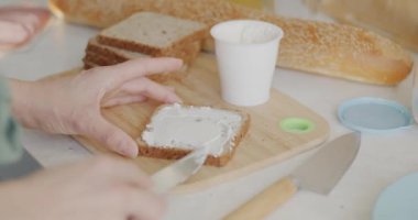 Kadın mutfaktaki masada ahşap tahtada lezzetli sandviçler pişirirken ellerin krem peyniri üzerine sürmesi. Gıda ve beslenme konsepti.