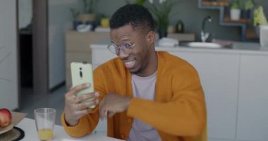 Akıllı telefon kamerasına poz veren ve evde eğlenirken selfie çeken Afro-Amerikalı adamın yavaş çekimleri. Fotoğraf ve insanlar konsepti.