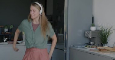 Kulaklıkla müzik dinleyen ve evde eğlenen mutlu genç bir kadın. Milenyum ve gençlik kültürü kavramı.