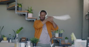Yavaş hareket eden neşeli Afrikalı Amerikalı adam etrafta dans ediyor ve evde kulaklıkla müzik dinliyor. İnsanlar ve eğlence konsepti.