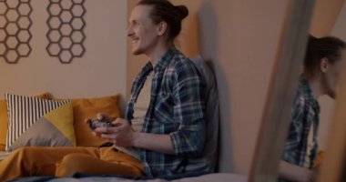 Oyun oynayan çok mutlu bir genç adam. Evde, yatak odasında oturup eğleniyor. Oyun ve eğlence konsepti.