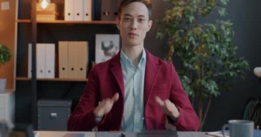 Neşeli genç iş adamı çevrimiçi video görüşmesi yapıyor. Kameraya bakıyor ve ofisin içinde konuşuyor. Profesyonel iletişim ve sanal buluşma kavramı.