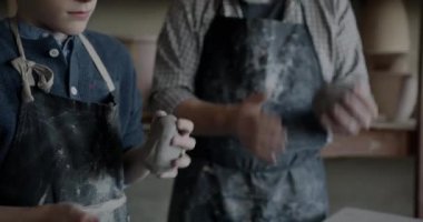 Oğlan ve kıdemli adam çömlek atölyesinde kil karıştırıyor ve atölyede yaratıcı aktivitelerin keyfini çıkarıyorlar. Kirli önlük giyen insanlar boş zamanlarında işlerine yoğunlaşırlar..