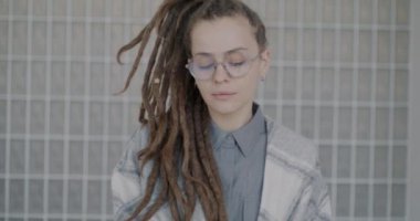 Rastalı genç bayanın yavaş çekimde çekilmiş bir portresi. İçeride cam duvara bakan kameraya bakıyor. İnsanlar ve tarz kavramı.