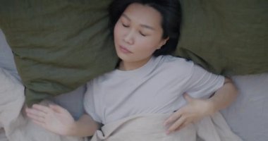 Ağır çekimde pijamalı Asyalı bir kadın yatakta uyuyor ve sabah evde dinleniyor. Uyku zamanı ve rahatlama kavramı.