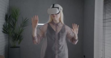 Sanal gerçeklik gözlüğü takan genç bir kadının evde yeni deneyimlerinin tadını çıkarması. Giyilebilir VR cihazı ve modern teknoloji konsepti.