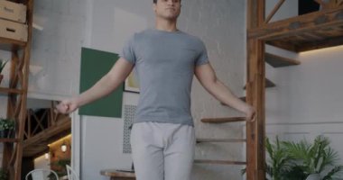 Aktif giyimli genç bir Orta Doğulu, atlama halatıyla atlıyor ve evde egzersiz yapıyor. Etkin yaşam tarzı ve ev içi spor pratiği kavramı.