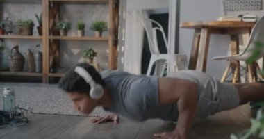 Orta Doğulu sporcu şınav çekiyor ve evde kablosuz kulaklıkla müzik dinliyor. Spor ve aktif yaşam tarzı kavramı.