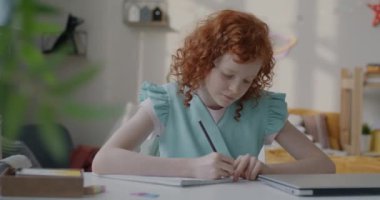 Not defterine yazı yazan akıllı küçük bir kızın yavaş çekimde evde oturup eğitime odaklanması. Çocukluk ve ev ödevi kavramı.