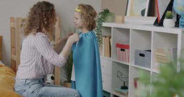 Koruyucu anne kılığındaki oğlu süper kahraman kostümü içinde çocuğunu öpüyor evde maskeli baloya hazırlanıyor. Çocukluk oyunu ve aile kavramı.