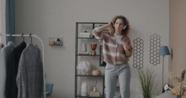 Aşırı neşeli genç kadının kulaklıkla müzik dinleyip evdeki yatakta dans etmesine odaklan. Eğlence ve gençlik kültürü kavramı.