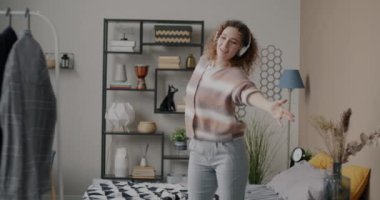 Kulaklıklı, dans eden ve yatak odasında müzik dinleyen neşeli bir kız. Eğlence ve insan konsepti.