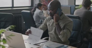 Profesyonel sohbete katılan Afro-Amerikalı işadamı cep telefonuyla konuşuyor ve ofiste belge okuyor. İş ve iletişim kavramı.