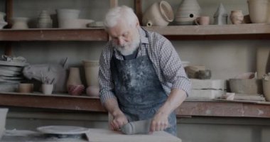 Yetenekli çömlekçi atölyede seramik ürünler yaratmak için kille çalışıyor. Kirli önlüklü yaşlı bir adam. Toprağı kabloyla kesiyor, sonra da malzemeyi karıştırıyor..