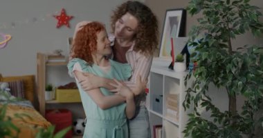Mutlu aile babasının yavaş çekimde çekilmiş bir portresi. Anne-kız kucaklaşıp gülümsüyor ve evde birlikte duran kameraya bakıyor. İnsanlar ve ilişki kavramı.