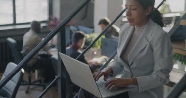 Orta Doğulu genç bir kadın modern ofis merdivenlerinde dizüstü bilgisayar kullanıyor. İş ve modern teknoloji kavramı.