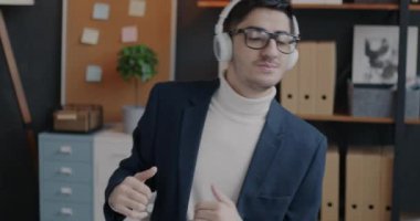 Orta Doğulu bir ofis çalışanı kablosuz kulaklıkla müzik dinliyor ve iş yerinde dans ediyor. İş ve eğlence konsepti.