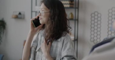 Cep telefonuyla konuşan mutlu Asyalı kadın gülümseyerek evde dostça sohbet ediyor. İletişim ve modern teknoloji kavramı.