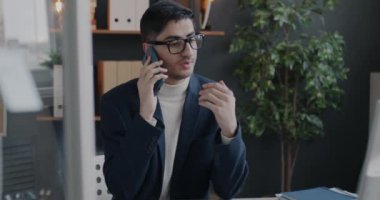 Orta Doğulu bir ofis çalışanı cep telefonuyla konuşuyor ve bilgisayarla iş yerinde profesyonel iletişim üzerine çalışıyor. İş ve cep telefonu bağlantısı kavramı.