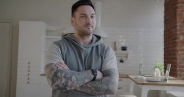 Kolları dövmeli, spor kıyafetli ve evde kameraya bakıp gülümseyen genç adamın yavaş çekim portresi. İnsanlar ve aktif yaşam tarzı kavramı.