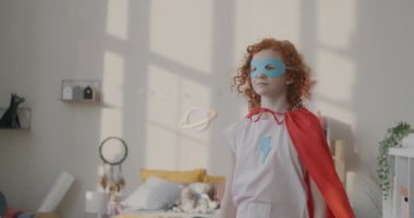 Maskeli ve pelerinli küçük bir kızın evde gülücükler saçarak oyun oynaması. Çocukluk ve eğlence kavramı.