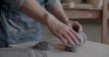 Erkek ellerinin çamurlu çalışma masasına kil atması stüdyoda sanat eseri yaratıyor. Çömlek atölyesi ve becerikli el emeği konsepti.