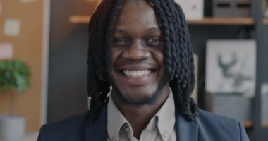 Ofiste kameraya gülümseyen neşeli Afro-Amerikan iş adamının yavaş çekim portresi. İş ve iyi ruh hali kavramı.