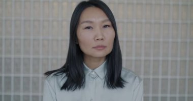 Camdan arka planda kameraya bakan düşünceli Asyalı kadının yavaş çekim portresi. Duygu ve ifade kavramı.