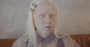 Lüks bir dairede şık kıyafetler içinde kameraya bakan genç albino kadının yavaş çekimde portresi. Bireysellik ve insanlar kavramı.