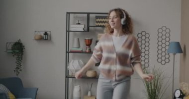 Yatak odasında eğlenen, kulaklıkla müzik dinleyen neşeli genç bayanın zoom portresi. İyi ruh hali ve gençlik kavramı.