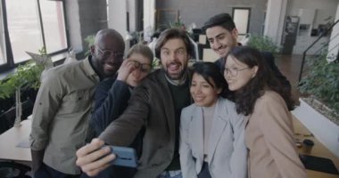 Ofiste eğlenen akıllı telefon kamerasıyla selfie çeken şakacı iş adamlarının ağır çekimleri. İş ve fotoğraf konsepti.