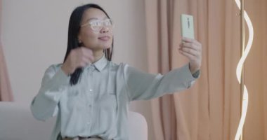 Lüks bir dairede akıllı telefon kamerası için selfie çeken şık Asyalı kadının yavaş çekimleri. Fotoğraf ve modern yaşam tarzı kavramı.