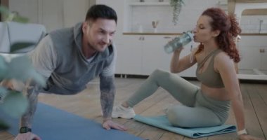 Erkek şınav çekerken kadın spor giyerken ve kocasıyla yoga minderinde konuşurken. Çift ve spor konsepti.