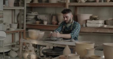 İş yerinde seramik demlik üreten önlüklü yetenekli bir adamın yavaş çekim portresi. Yaratıcı adam geleneksel mesleği seviyor. Küçük işletmeler kuruyor..
