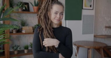 Modern apartman dairesinde dikilen yaratıcı saç stiliyle gülümseyen güzel genç bayan portresi. Pozitif duygu ve bireysel tarz kavramı.