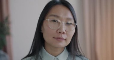 Yakın çekimde, bulanık apartman arka planına bakan gülümseyen Asyalı kadının yavaş çekim portresi. İyi ruh hali ve insan konsepti.