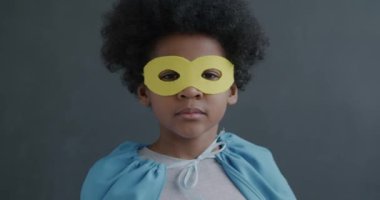 Gri arka planda süper kahraman kostümü giymiş kendine güvenen Afrikalı Amerikalı çocuğun yakın çekim yavaş portresi. Çocukluk ve karakter kavramı.