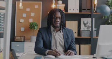 Not defterinde bilgisayar yazısıyla çalışan ve ofisinde akıllı telefon kullanan hırslı Afro-Amerikan iş adamının yakınlaştırılması. İş ve iş kavramı.