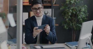 Neşeli Ortadoğulu iş adamı internet üzerinden video oyunu oynuyor. Akıllı telefon ofis odasında dinleniyor. Eğlence ve oyun konsepti.